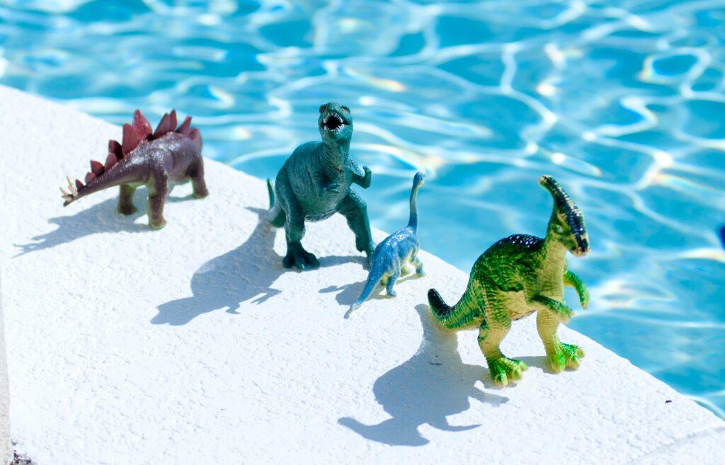 three green and gray animal figurines on white sand during daytime