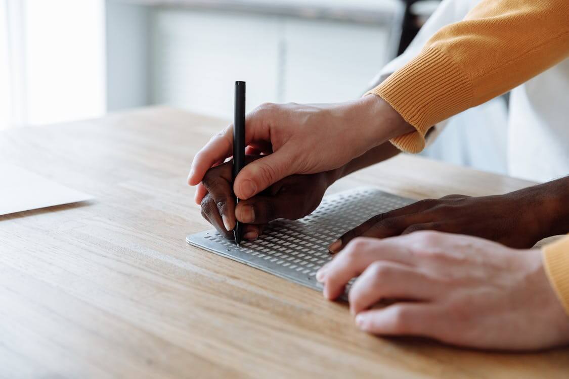 Free Hands skillfully guiding a student in learning braille on an embossed board. Stock Photo